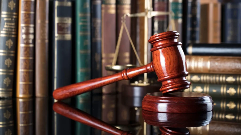 A close-up of a wooden gavel with law books and a scale in the background.