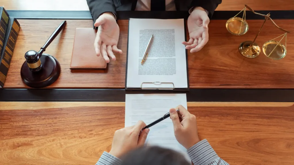 Two people discussing a legal document across a wooden desk.